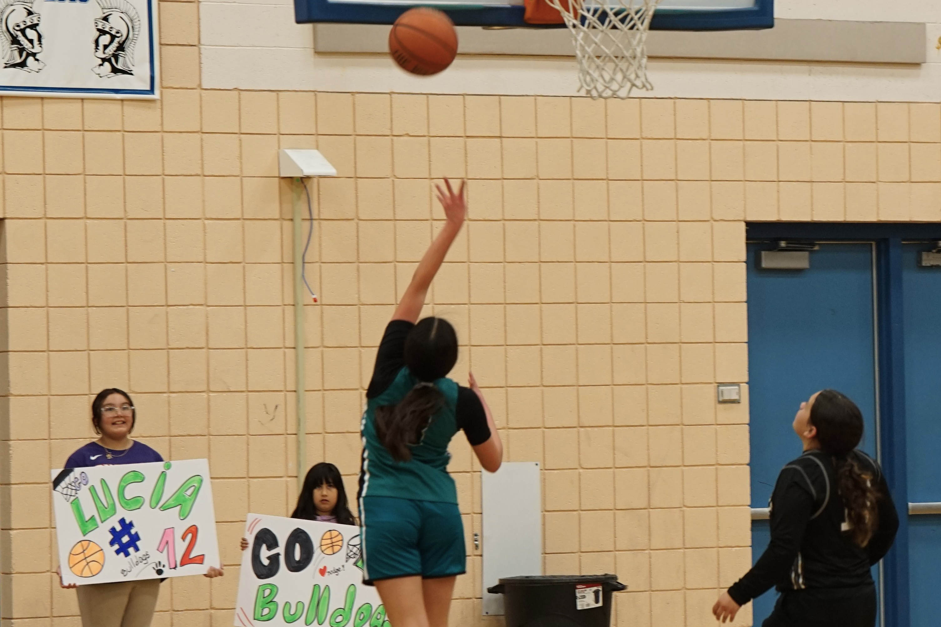 A Bulldogs player goes in for a layup while two girls hold up posters cheering the team on