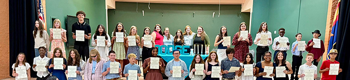 Middle school students hold up certificates