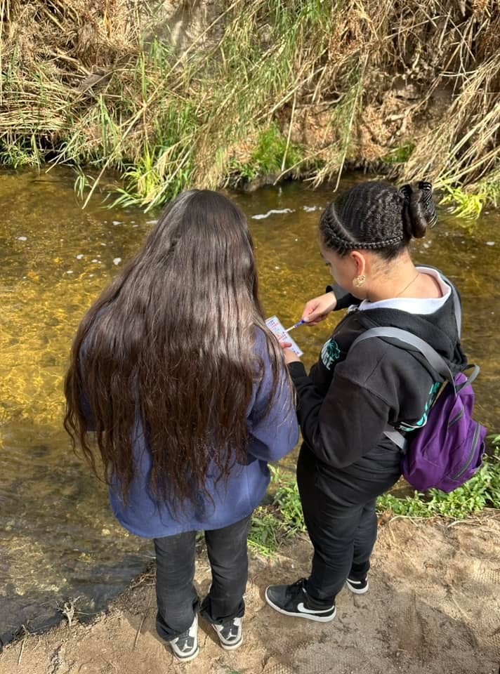 Two girls stand on the riverbank conducting research