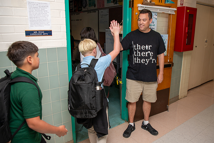 A man high-fives his students as they walk into the classroom