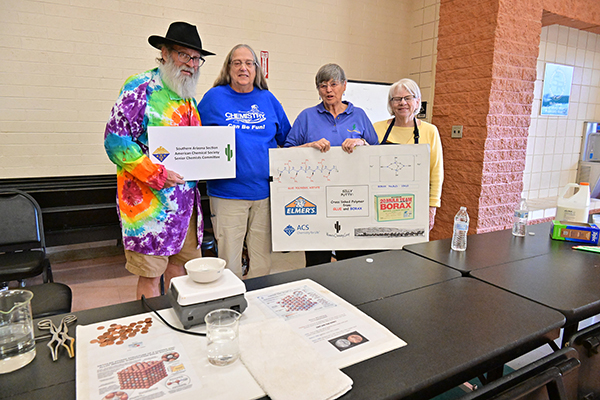 A group of 1 man and three women hold up signs for their chemistry table