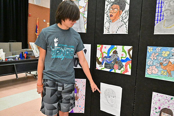 A preteen boy points to his artwork on display