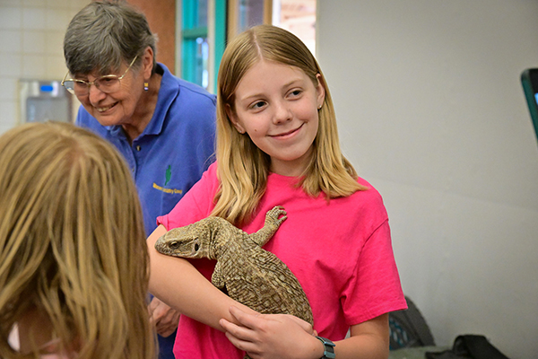 A preteen girl smiles as she holds a giant lizard