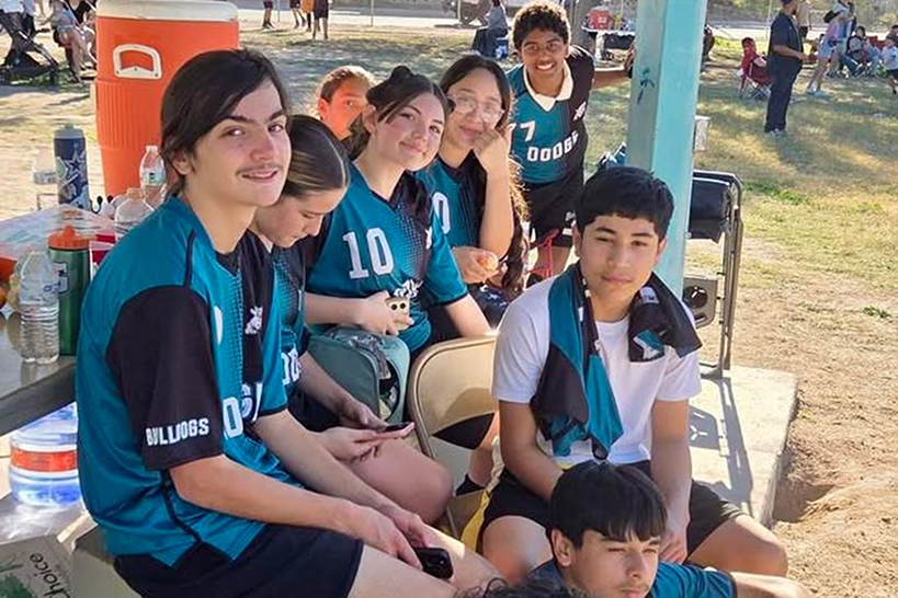 The flag football team sits on a picnic table on the sidelines