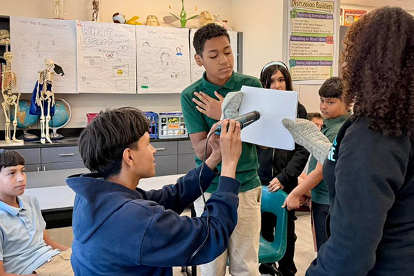 Students hold a piece of paper with oven mitts while another student points a heat ray at it