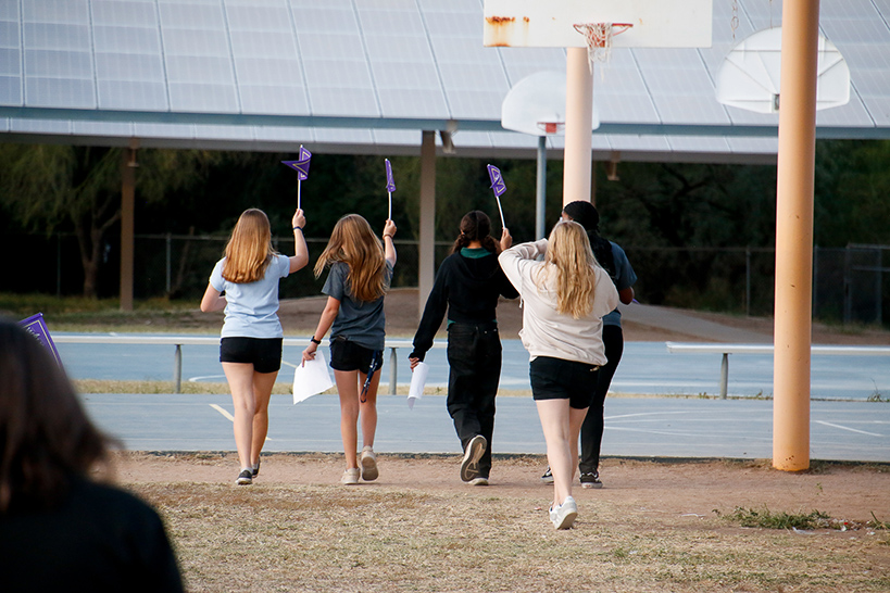A group of preteen girls walk across the outdoor basketball court holding up purple Ruby Bridges pennants
